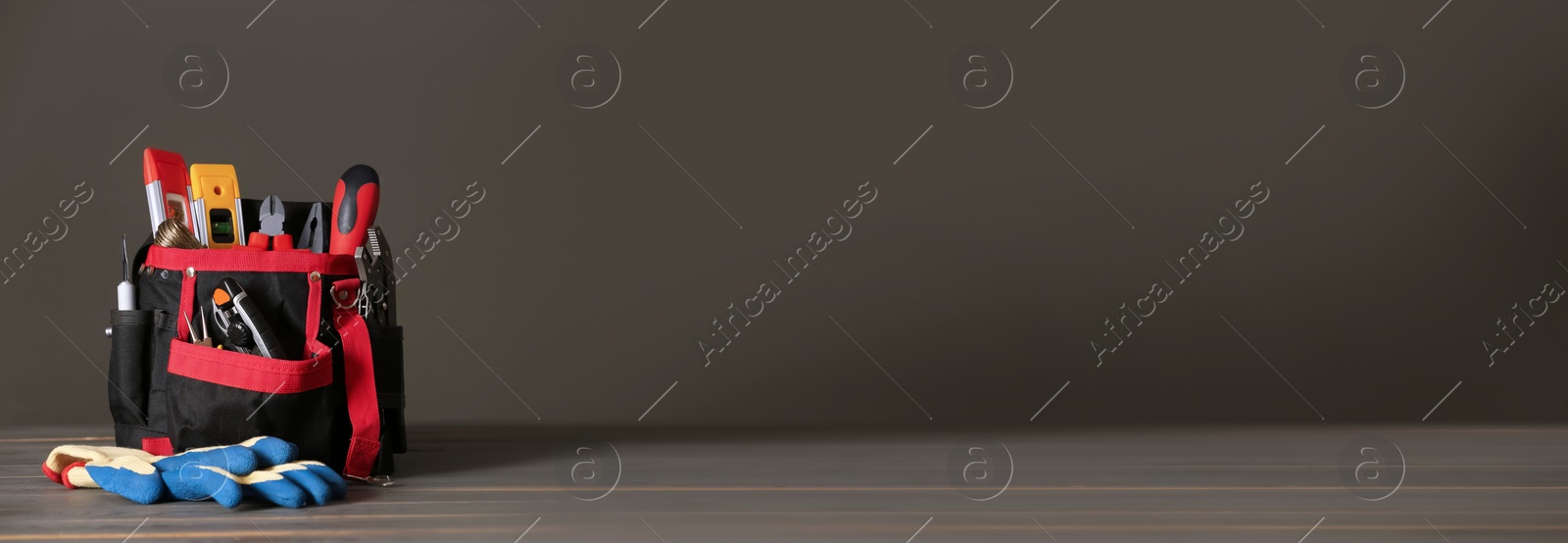 Image of Bag with different tools for repair and protective gloves on grey wooden table, space for text. Banner design