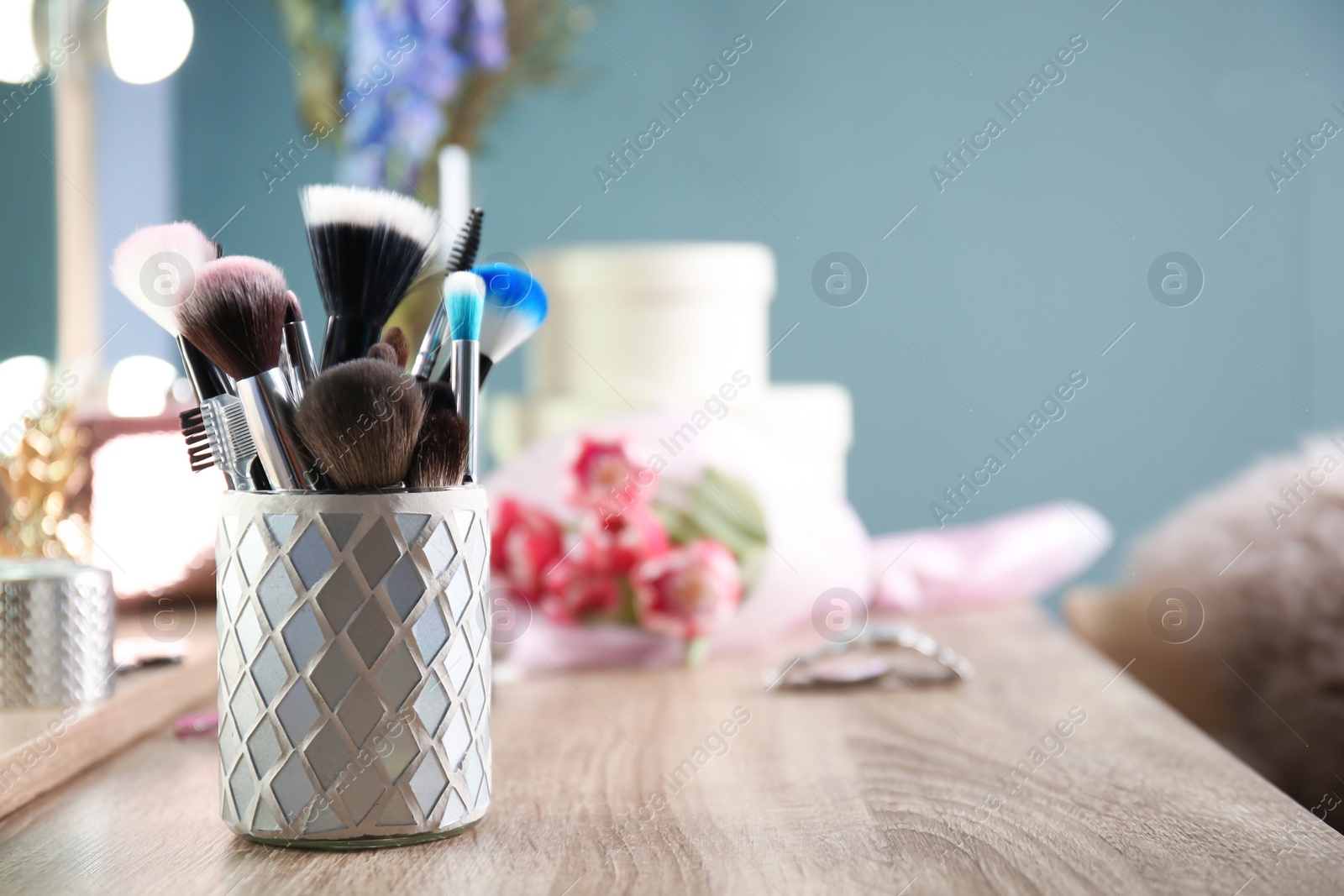 Photo of Holder with professional makeup brushes on wooden table