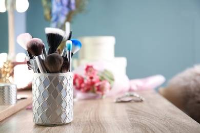 Holder with professional makeup brushes on wooden table