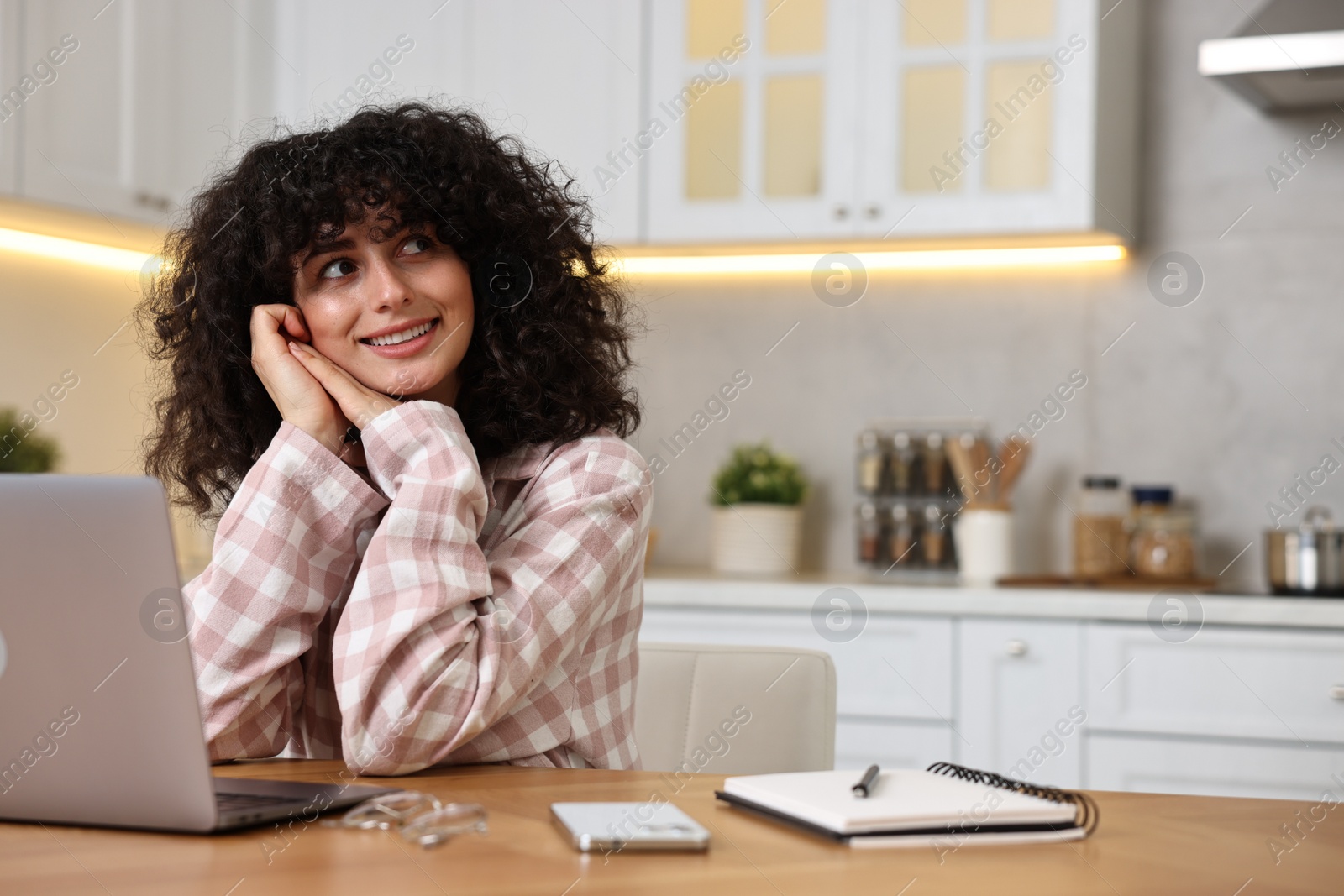 Photo of Beautiful young woman in stylish pyjama with laptop at wooden table in kitchen