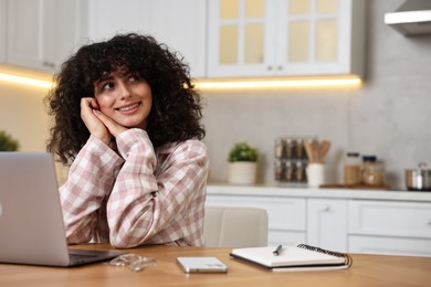 Beautiful young woman in stylish pyjama with laptop at wooden table in kitchen