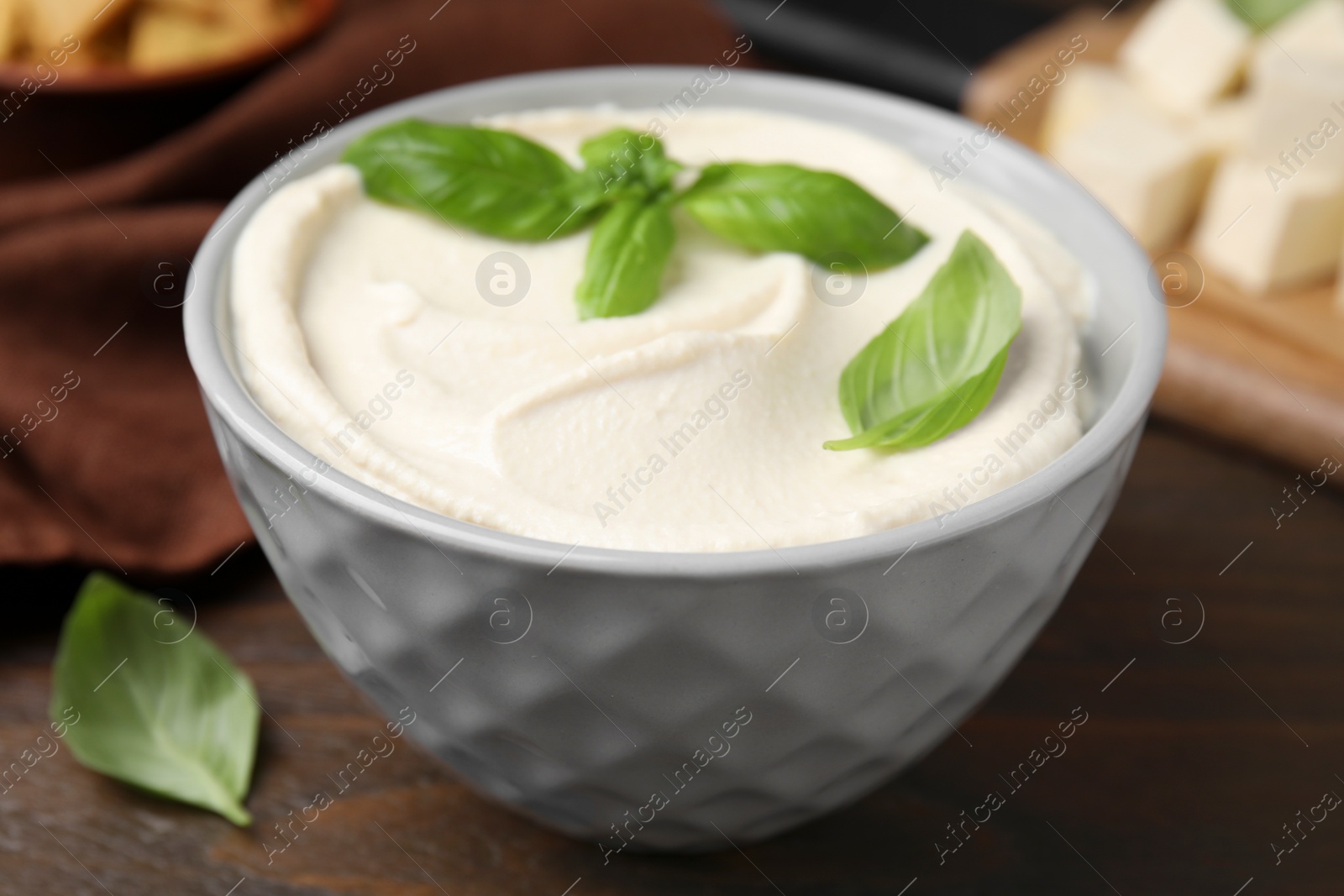 Photo of Delicious tofu sauce and basil leaves in bowl on wooden table, closeup