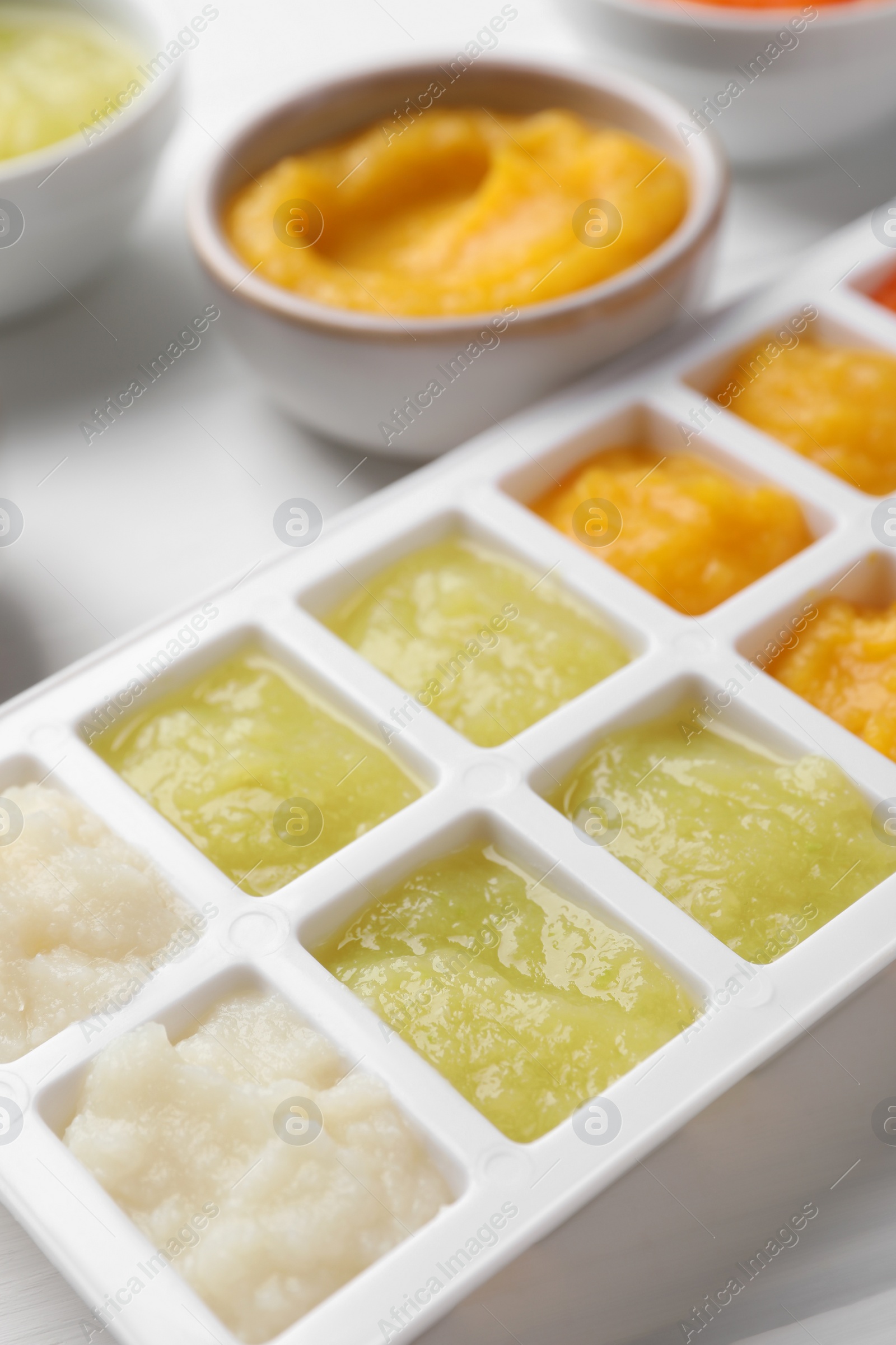 Photo of Different purees in ice cube tray on white table, closeup. Ready for freezing