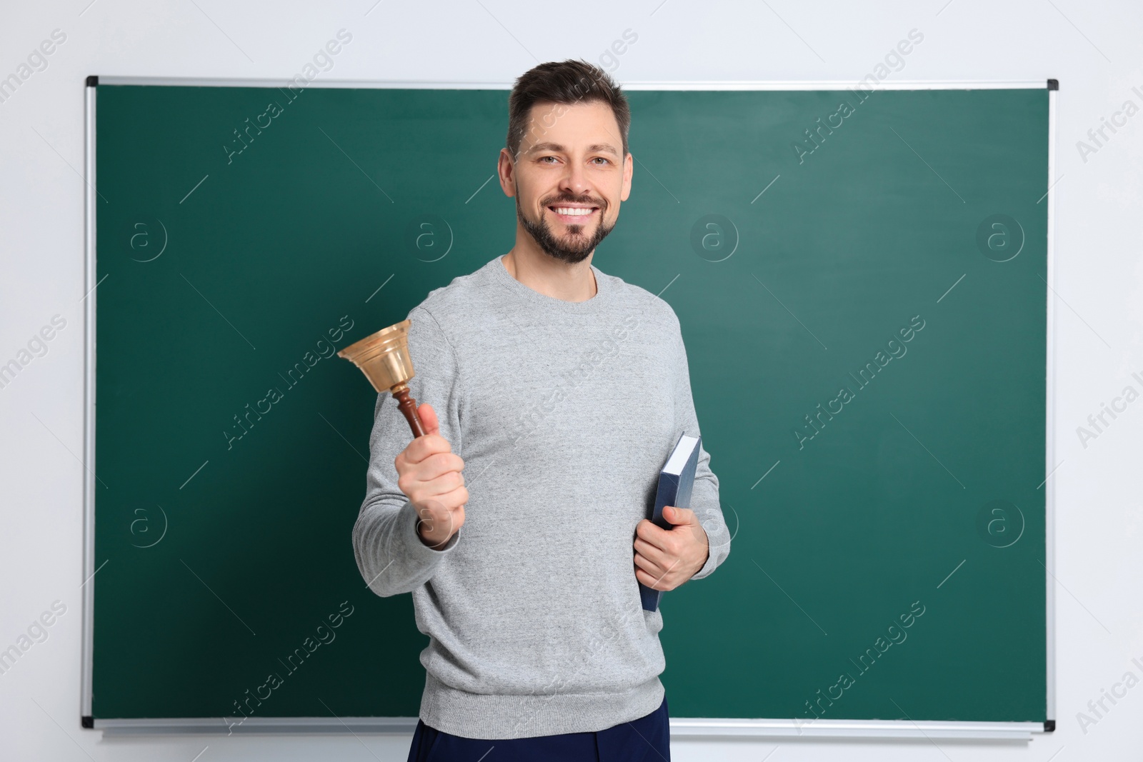 Photo of Teacher with school bell near chalkboard indoors. Space for text