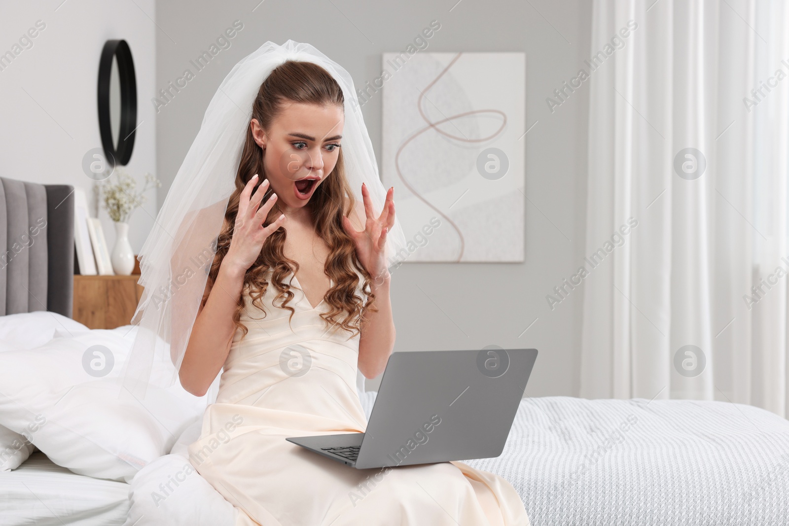 Photo of Shocked bride with laptop on bed in bedroom