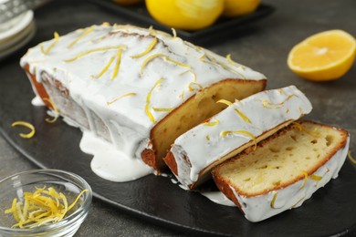 Photo of Tasty lemon cake with glaze, citrus fruits and zest on table, closeup