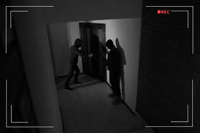 Dangerous criminals with gun and crow bar intruding into apartment, view through CCTV camera