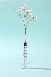 Cosmetology. Medical syringe and gypsophila on light blue background