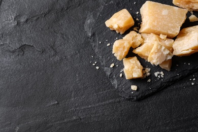 Photo of Pieces of delicious parmesan cheese on black table, top view. Space for text