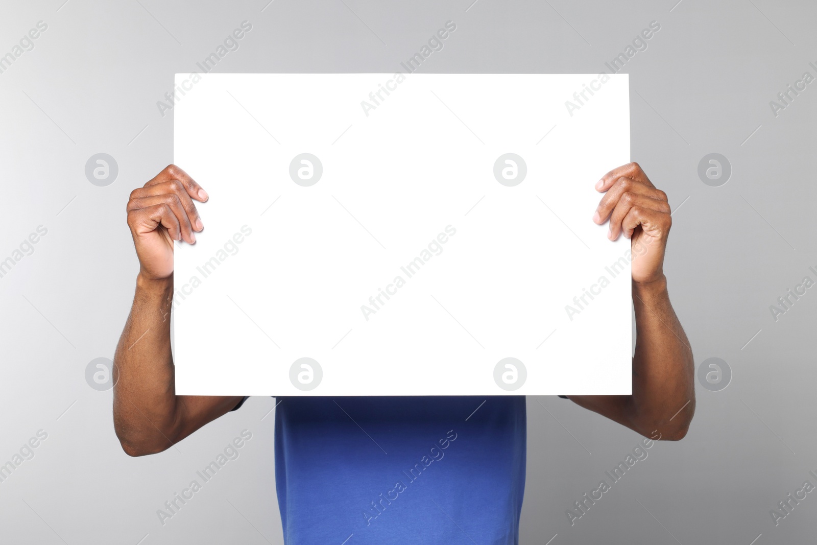 Photo of African American man holding sheet of paper on grey background. Mockup for design