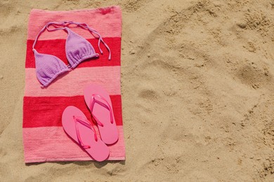 Photo of Beach towel with slippers and swimsuit on sand, top view. Space for text