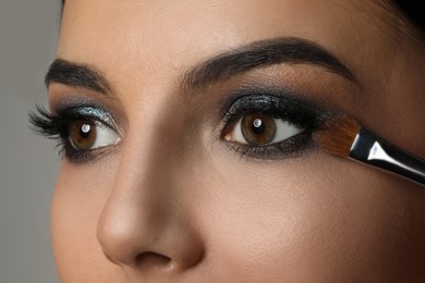 Photo of Applying dark eye shadow with brush onto woman's face, closeup. Beautiful evening makeup