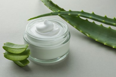 Photo of Jar with cream and cut aloe leaves on light grey background, closeup
