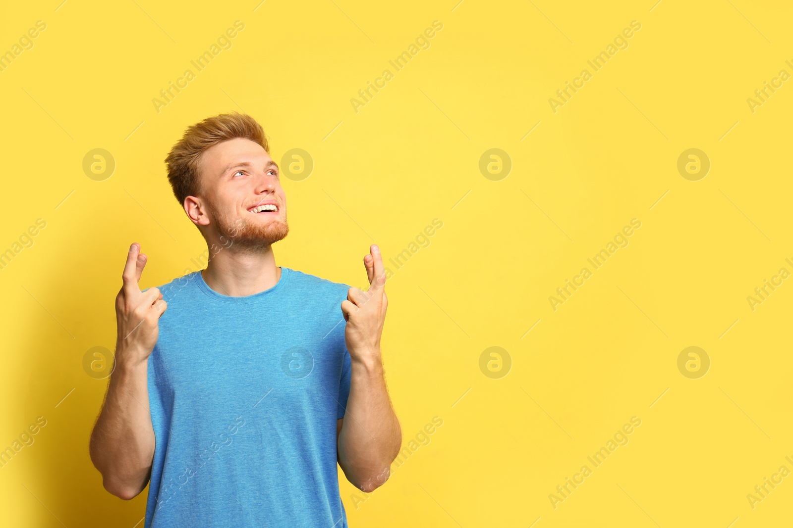 Photo of Portrait of hopeful man with crossed fingers on yellow background, space for text