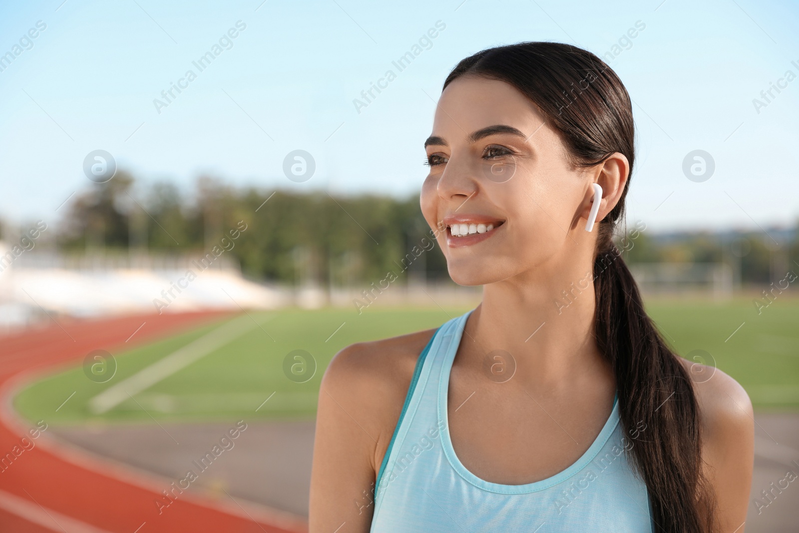 Photo of Young sportswoman with wireless earphones at stadium