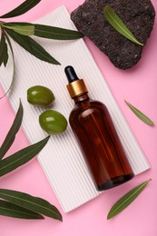 Photo of Cosmetic products with olive essential oil, stone and leaves on pink background, flat lay
