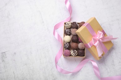 Photo of Open box with delicious chocolate candies and pink ribbon on white table, top view. Space for text