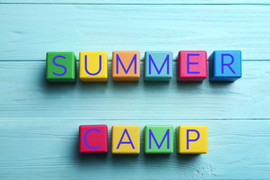 Photo of Phrase SUMMER CAMP made with colorful cubes on light blue background, flat lay