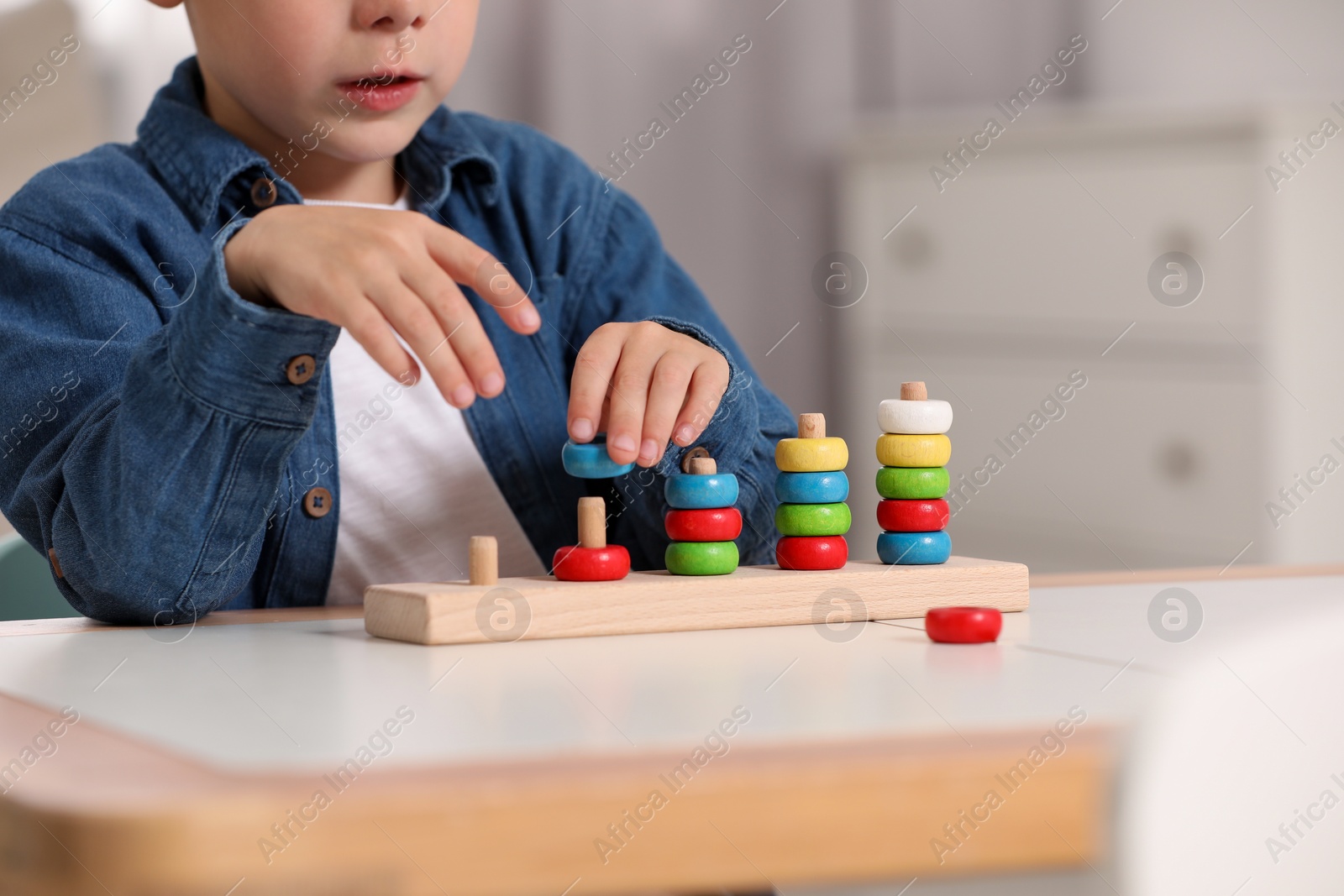 Photo of Little boy playing with stacking and counting game at table indoors, closeup. Child's toy