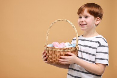Photo of Easter celebration. Cute little boy with wicker basket full of painted eggs on dark beige background. Space for text