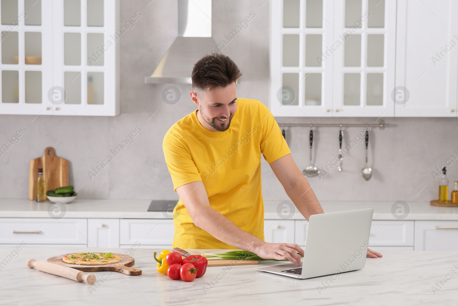 Photo of Man watching cooking online course on laptop while making pizza in kitchen. Time for hobby