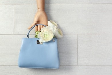 Flat lay composition of stylish bag with spring flowers and mannequin hand on wooden background. Space for text