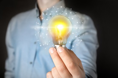 Image of Glow up your ideas. Man holding light bulb on dark background, closeup