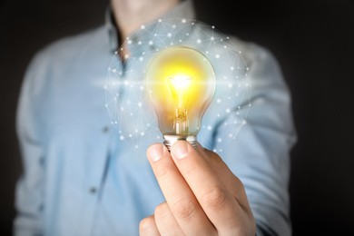 Glow up your ideas. Man holding light bulb on dark background, closeup