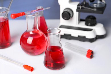 Photo of Laboratory analysis. Glass flasks with red liquid and microscope on white table indoors