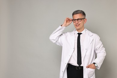 Happy doctor in glasses on grey background, space for text