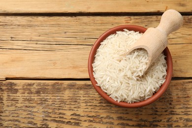 Photo of Raw basmati rice and scoop in bowl on wooden table, top view. Space for text