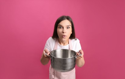 Emotional young woman with cooking pot on pink background