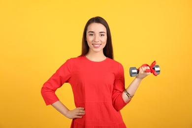 Photo of Woman with dumbbell as symbol of girl power on yellow background. 8 March concept