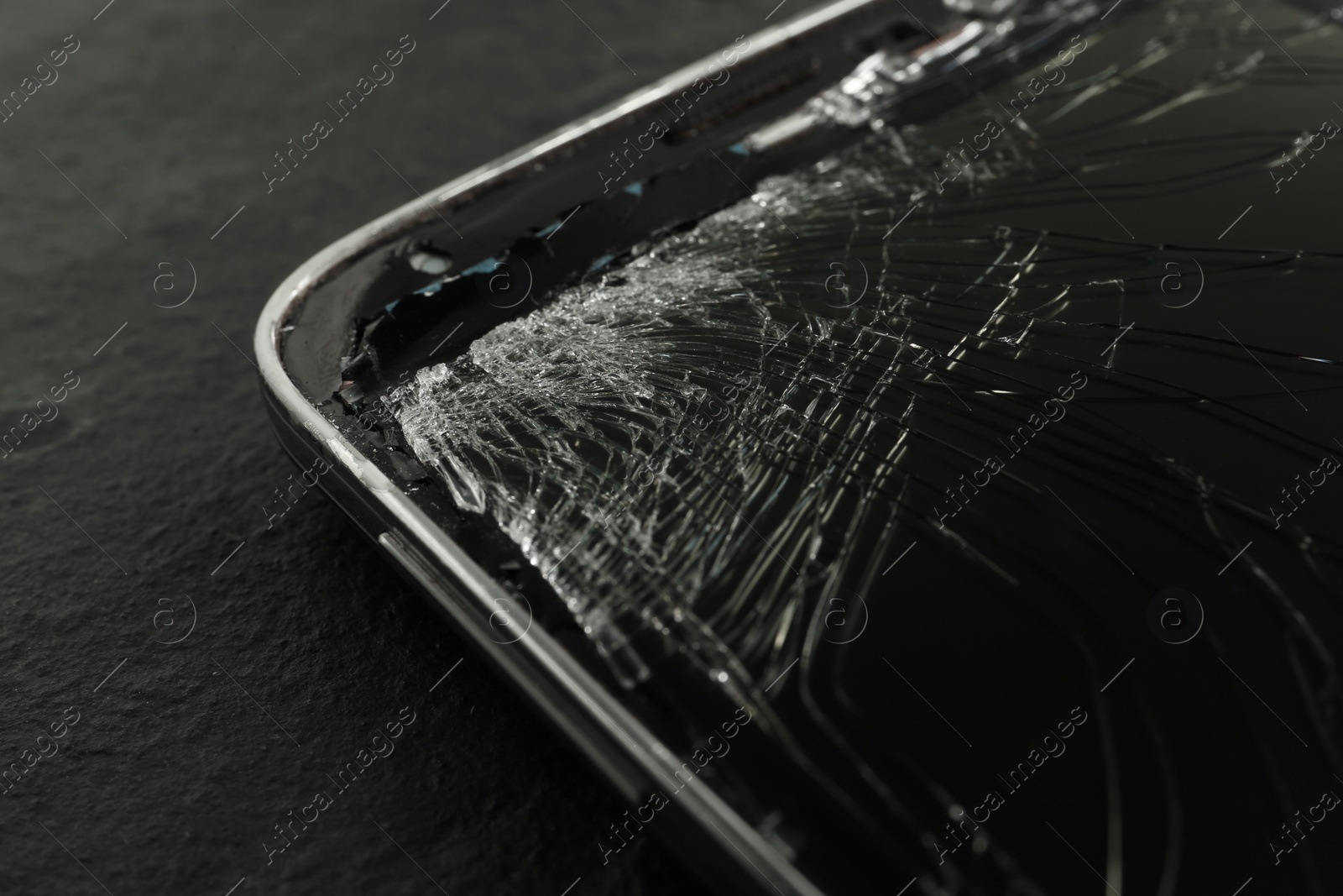 Photo of Smartphone with cracked screen on black table, closeup. Device repair