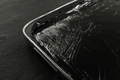 Smartphone with cracked screen on black table, closeup. Device repair