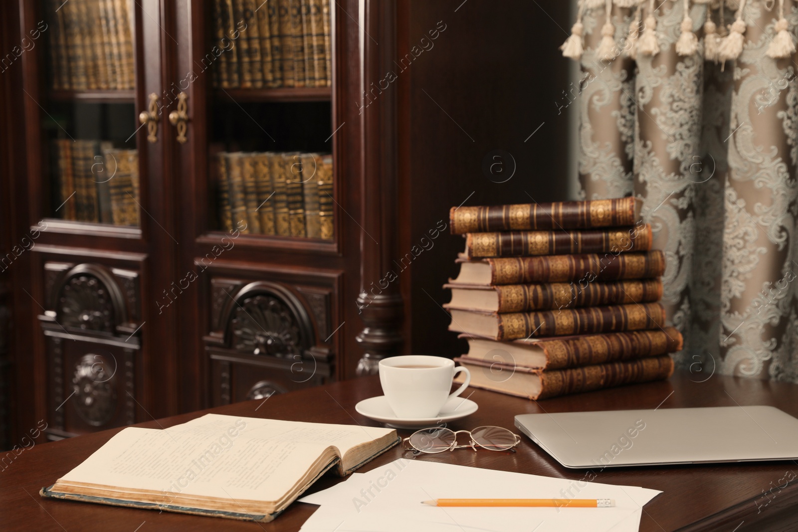 Photo of Laptop, books and cup of coffee on wooden table in library reading room