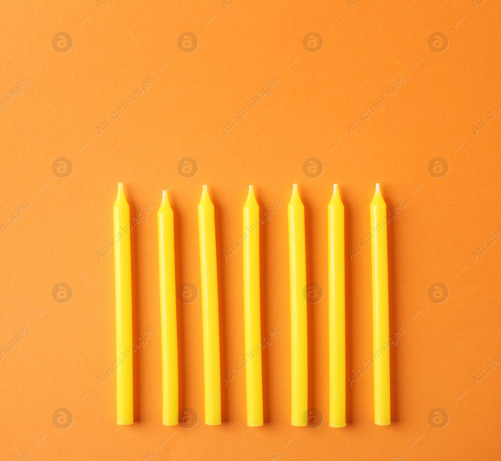 Photo of Yellow birthday candles on orange background, top view