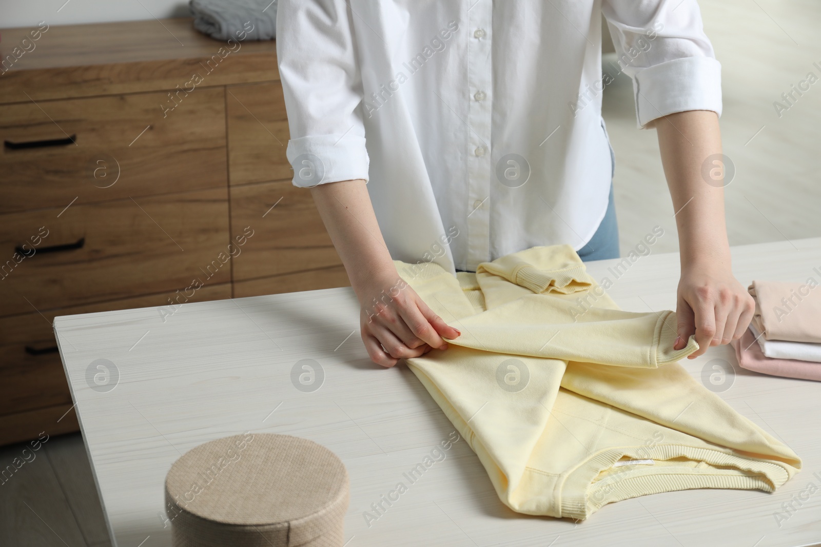 Photo of Woman folding clothes at white wooden table indoors, closeup