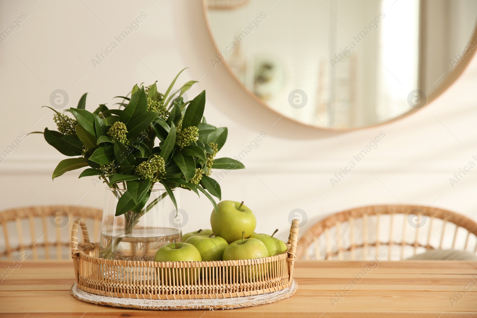 Photo of Fresh plant branches with green leaves near apples on wooden table indoors