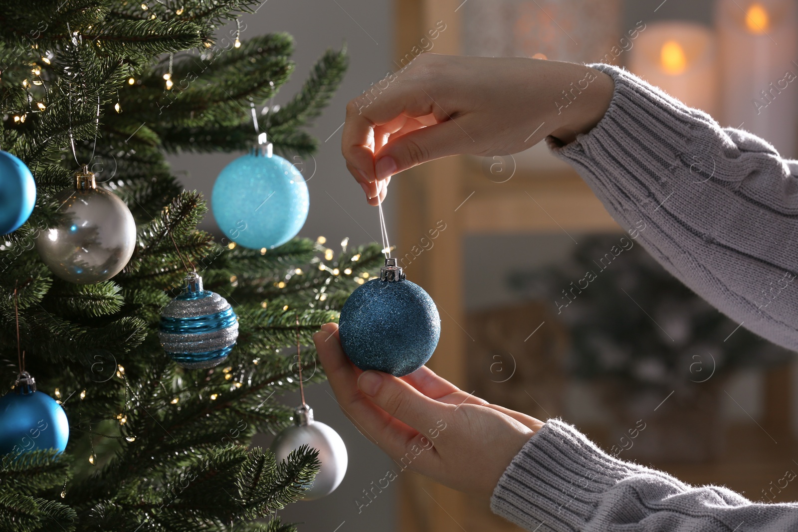 Photo of Woman decorating Christmas tree with shiny ball indoors, closeup