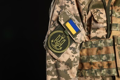 Photo of Soldier with Ukrainian flag and trident on military uniform against black background, closeup