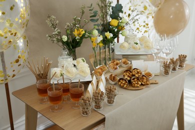 Photo of Tasty treats and glasses of drink on table in room. Sweet buffet