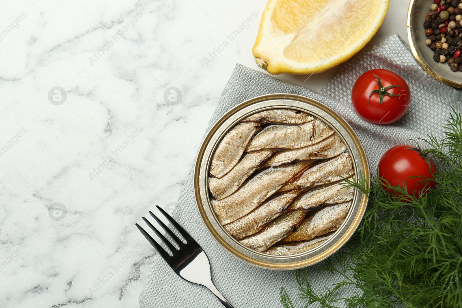 Photo of Tin can with tasty sprats served on white marble table, flat lay. Space for text