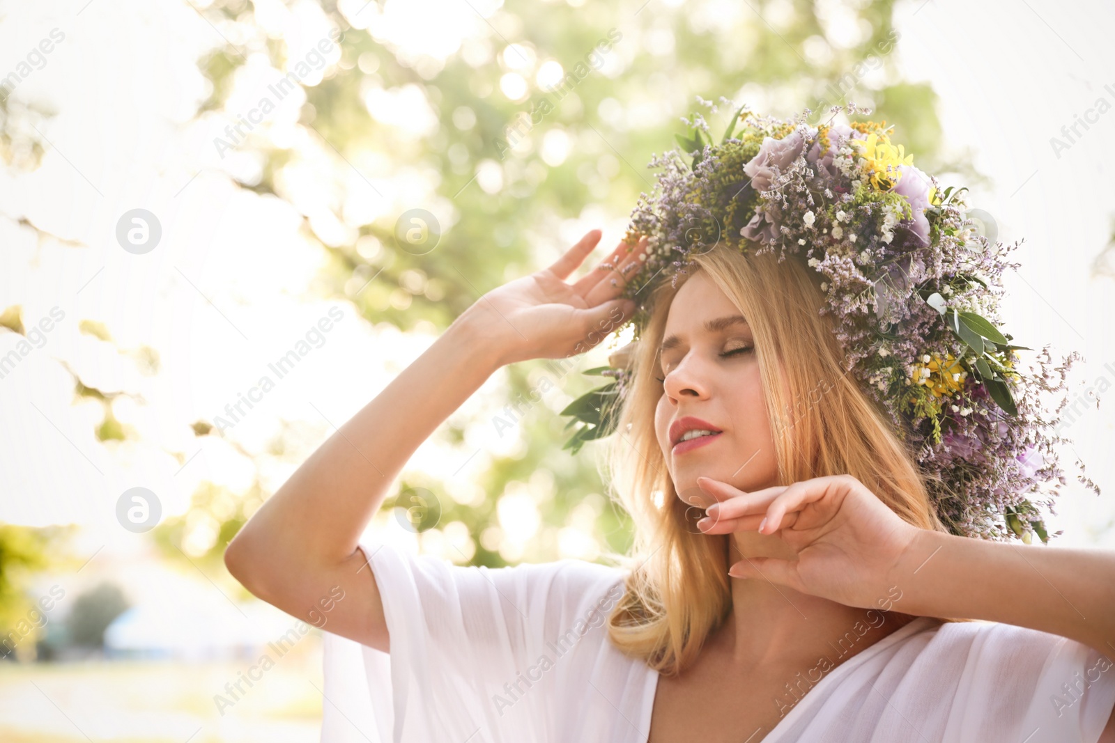 Photo of Young woman wearing wreath made of beautiful flowers outdoors on sunny day