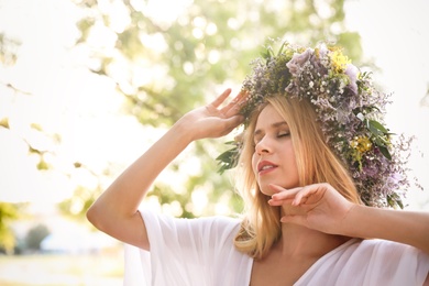 Young woman wearing wreath made of beautiful flowers outdoors on sunny day