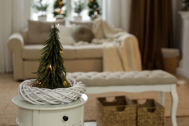 Photo of Small decorative Christmas tree on white table in living room. Interior design