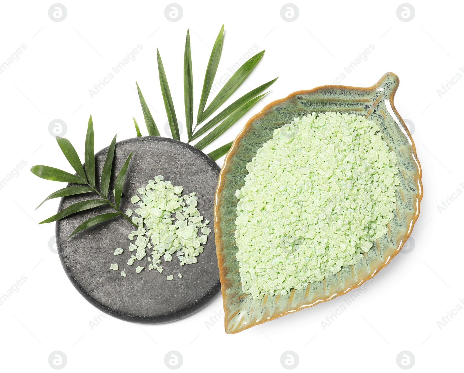 Photo of Green sea salt in bowl, spa stone and palm leaves isolated on white, top view
