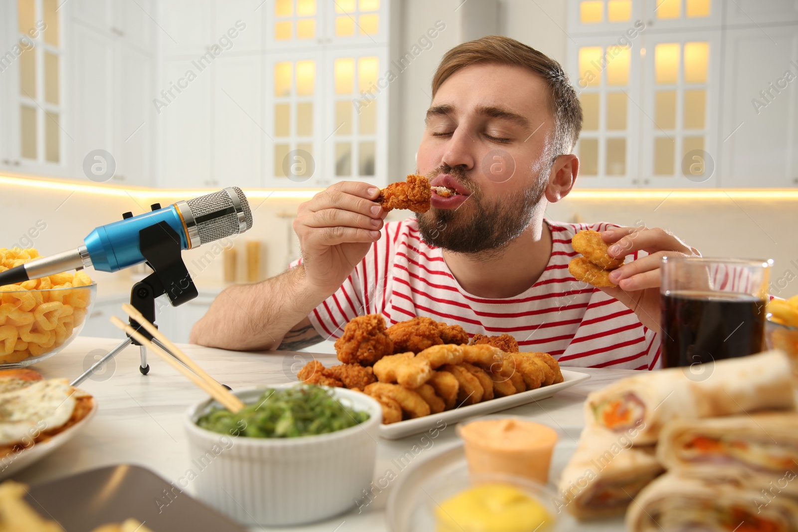 Photo of Food blogger eating near microphone at table in kitchen. Mukbang vlog