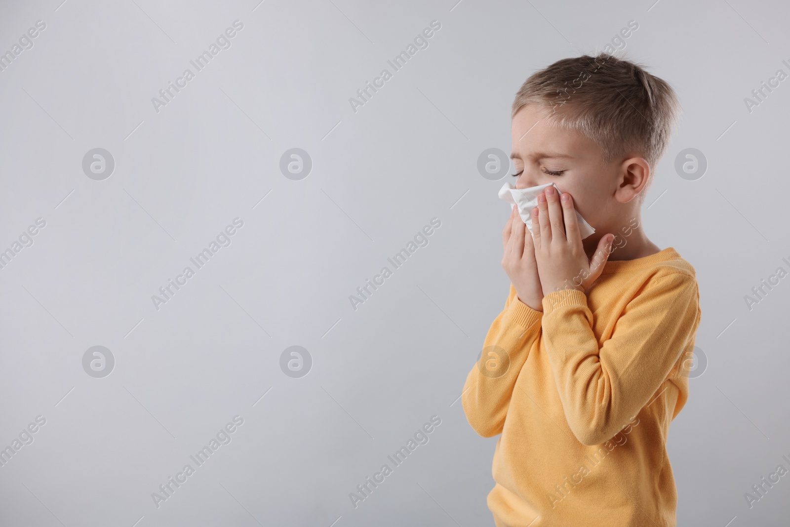 Photo of Sick boy with tissue coughing on gray background, space for text. Cold symptoms