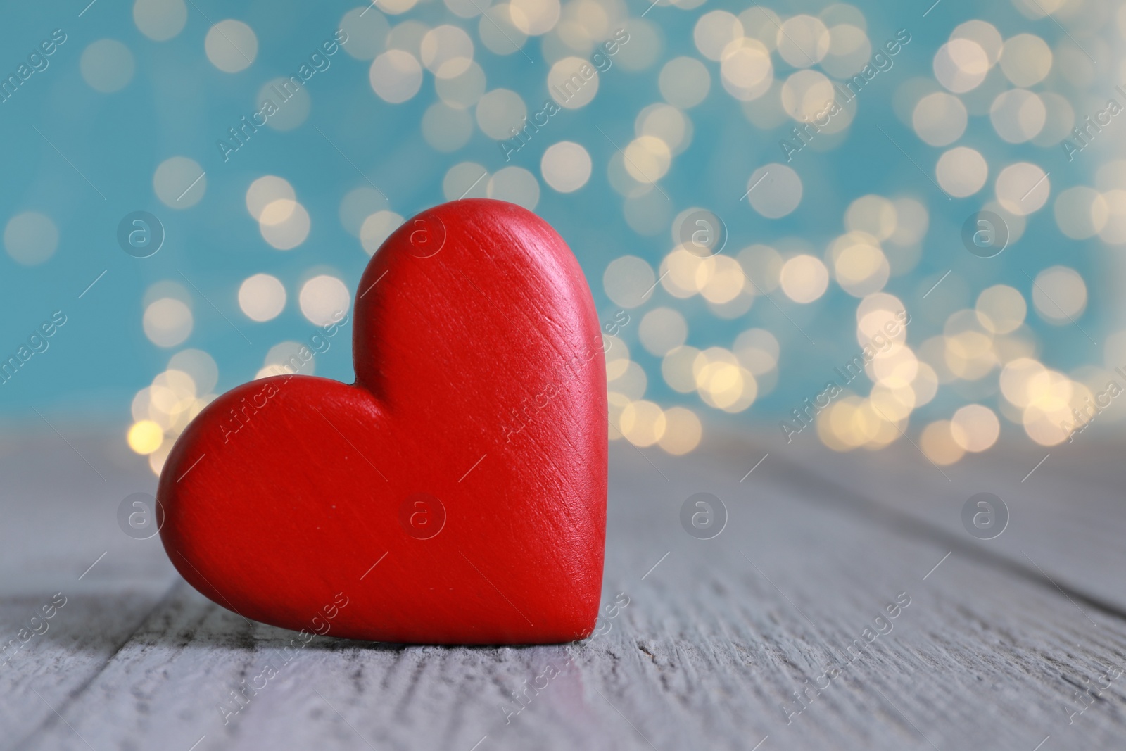 Photo of Red decorative heart on grey wooden table against blurred lights, closeup